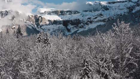 una vista aérea del cirque du fer à cheval mientras está cubierto de nieve durante un frío invierno, inclinándose hacia arriba desde la carretera para revelar la inmensidad del bosque apostado a los pies del épico circo