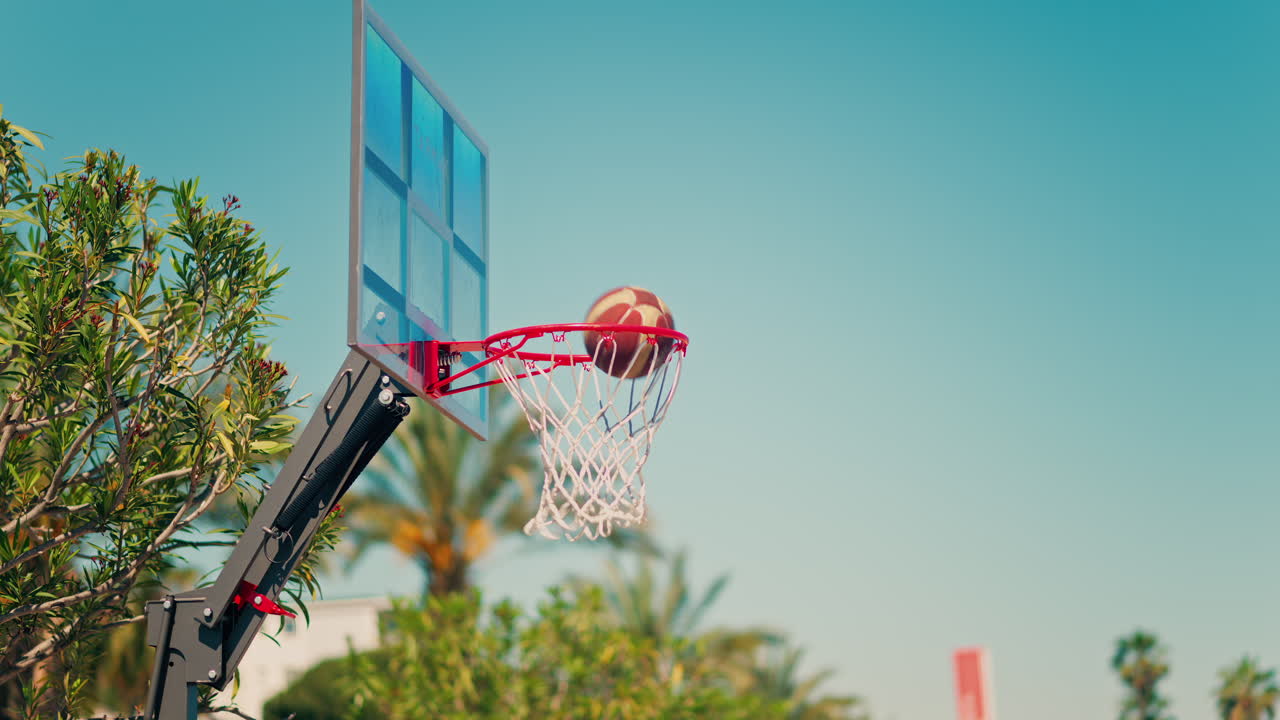 Antibes, France - May 10, 2025: Two basketballs going through the net with palm trees on the background