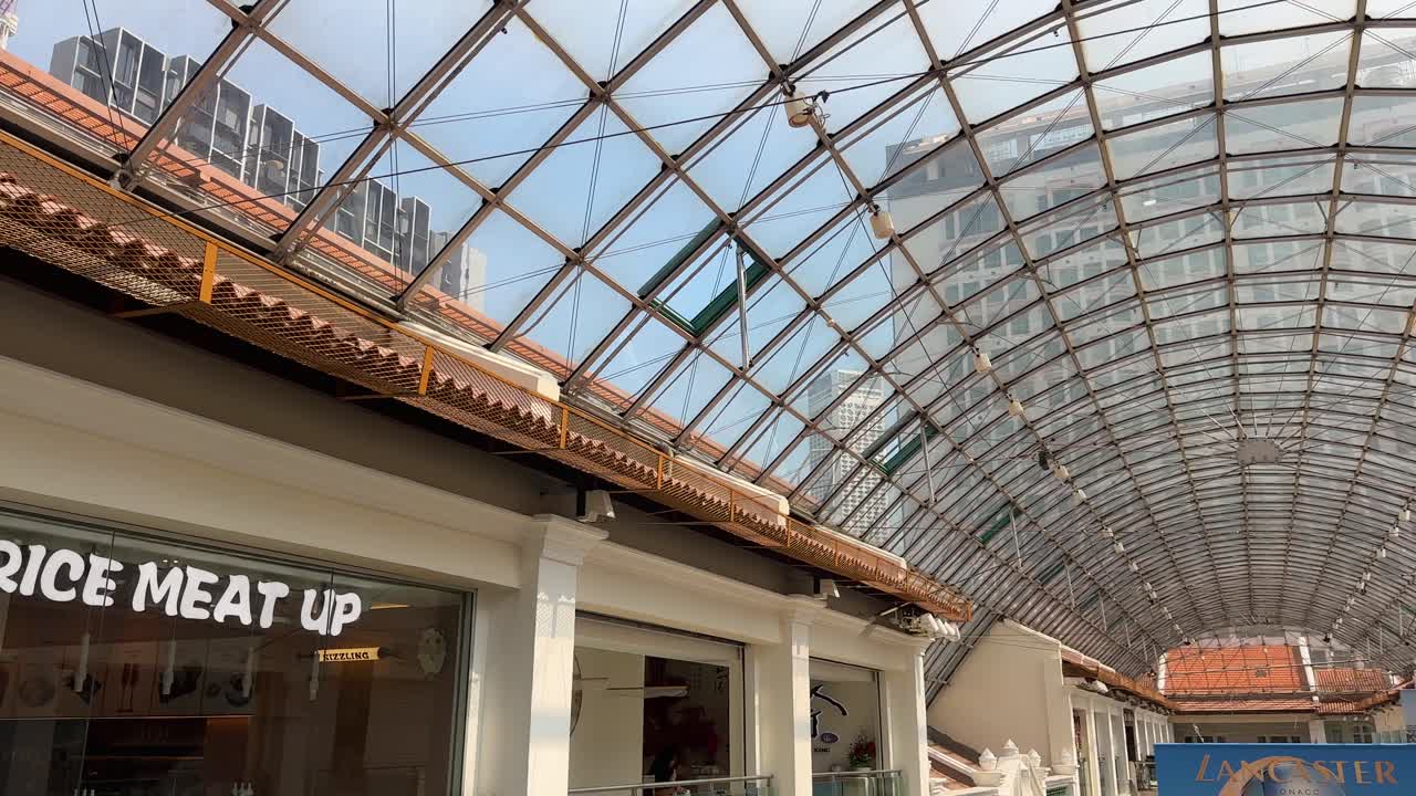 Glass-roofed shopping mall with closed stores, bright daylight, and architectural details in Singapore