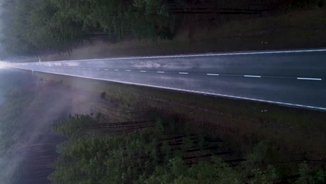 aerial vertical descending shot over the asphalt road in the foggy forest with mist - horror, dark scenery concept