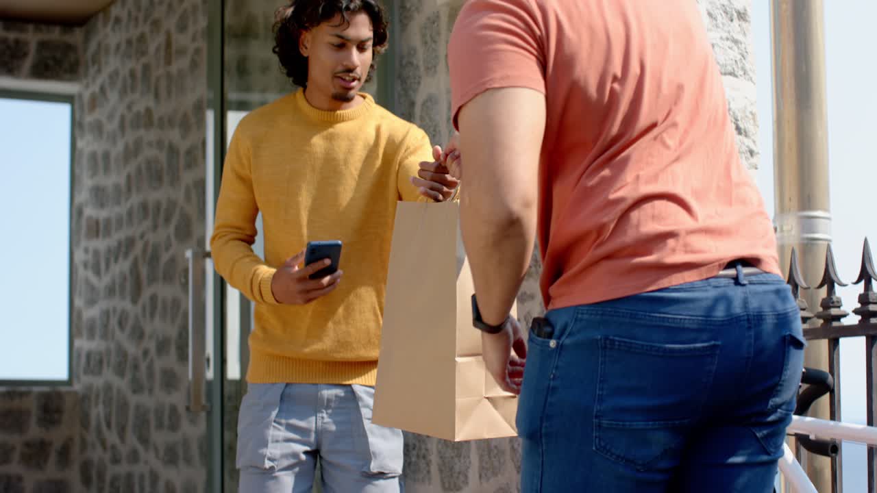 Courier arriving with red bag to customer with smartphone, unzipping and handing brown bag on porch