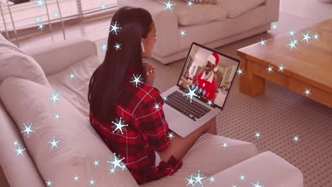 Animation-of-snow-falling-over-mixed-race-woman-on-laptop-video-call-with-santa-at-christmas
