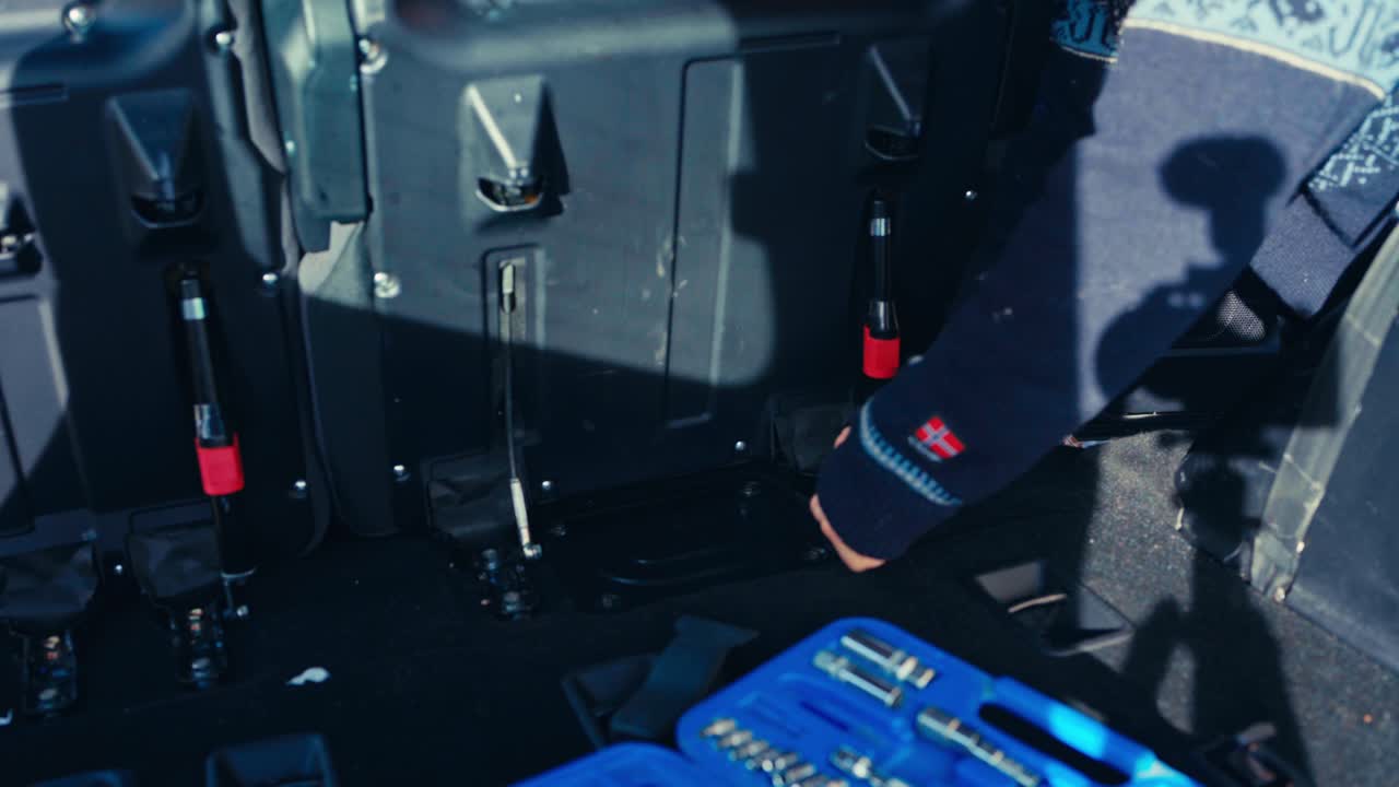 A Man is Using a Ratchet Wrench to Loosen the Bolts on the Rear Seat Base to Modify the Pajero's Interior - Close Up