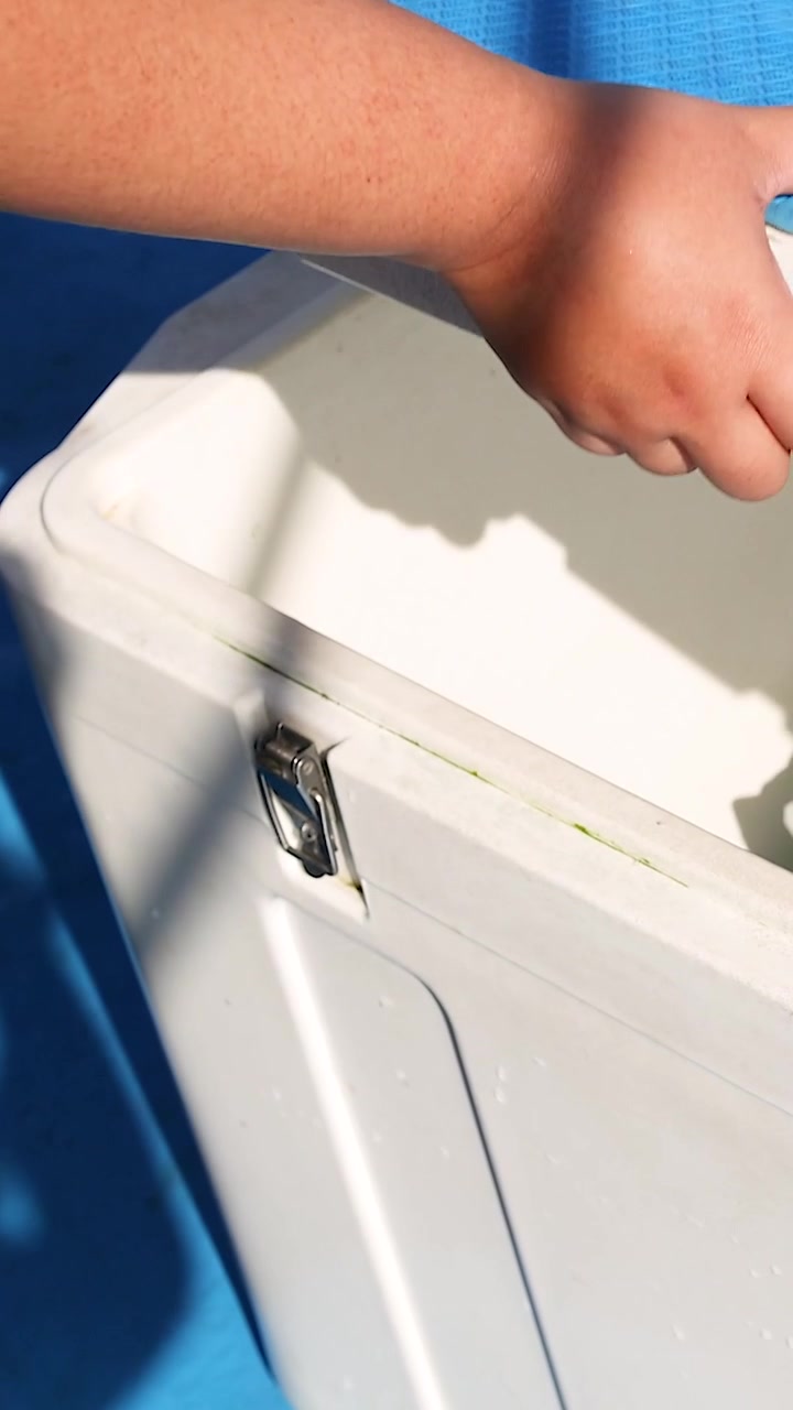 A person opens an ice box filled with ice and drinks under bright sunlight in Phuket, Thailand