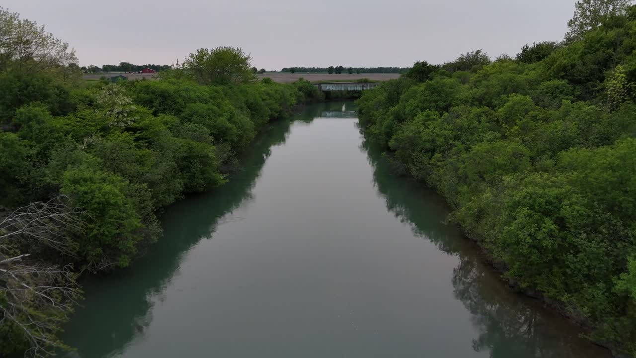 Drone volant à basse altitude à travers un canal se terminant à un pont ferroviaire avec des champs en arrière-plan