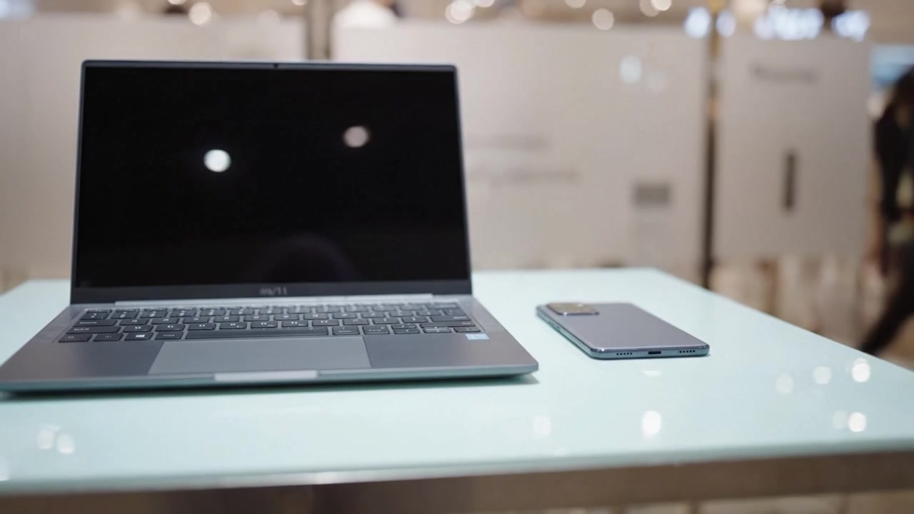 Spazio di lavoro moderno con un laptop elegante e uno smartphone su una superficie di vetro, catturato in due inquadrature per un'estetica tecnologica raffinata.