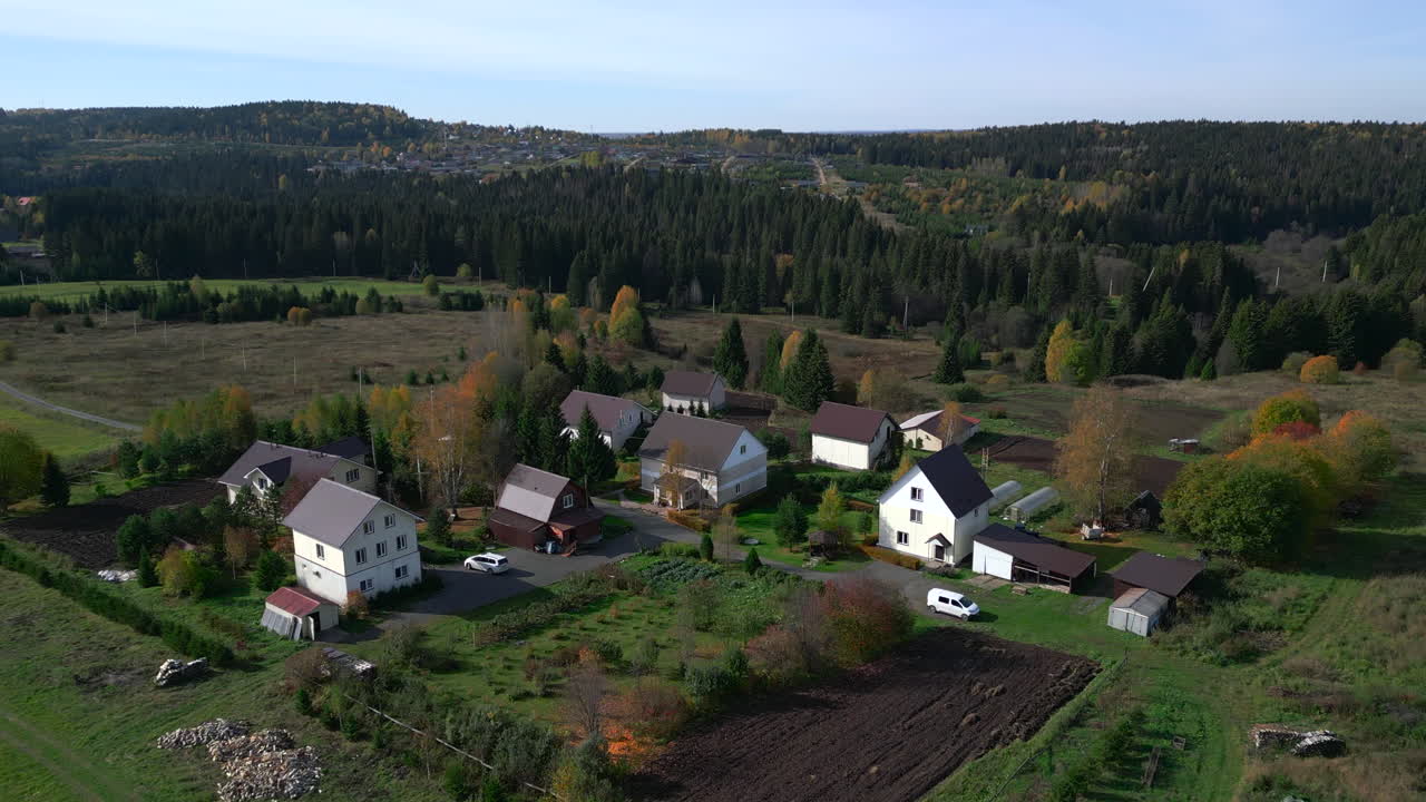 Luftfoto av landlige hus og jorder, mot en skogkledd horisont i rolig høstlys, droneopptak. Klipp.