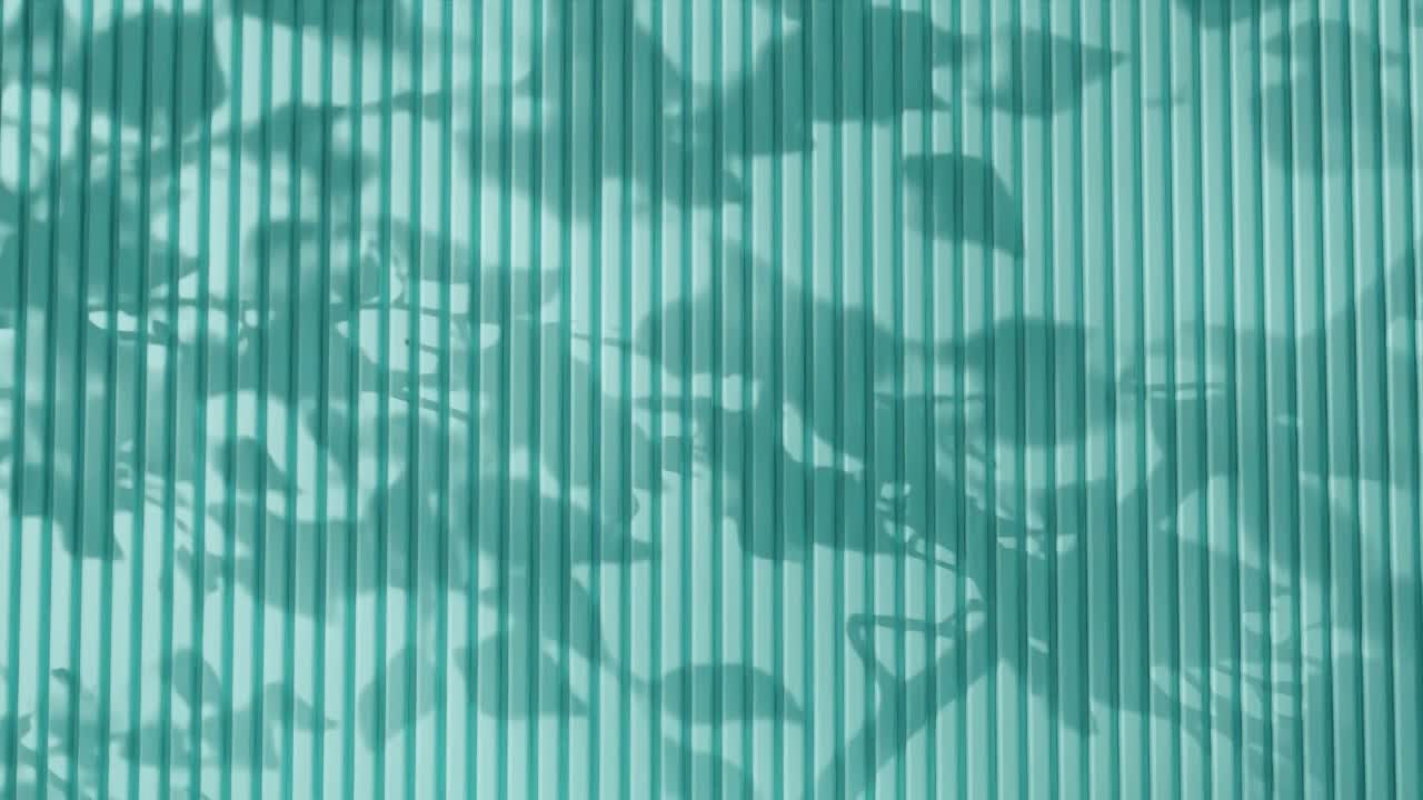 Shadow of tree branches and leaves on vertical green corrugated metal wall. Abstract natural light and linear pattern background. Design for wallpaper, banner, postcard, greeting card, poster, header.
