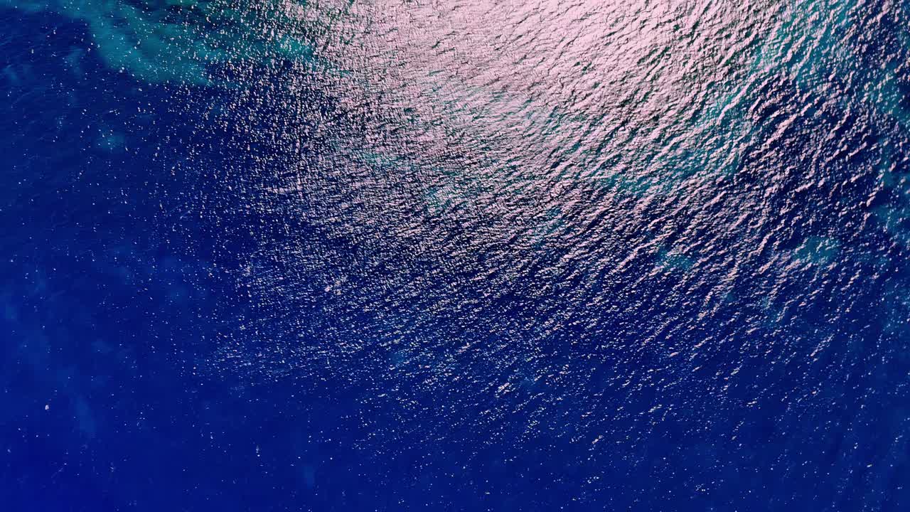 Vista aerea dall'alto della scintillante superficie del profondo blu del Mar Mediterraneo con il riflesso dorato del sole vicino a Gozo, Malta, durante una luminosa giornata estiva di sole, catturata con cinematografia professionale tramite drone.