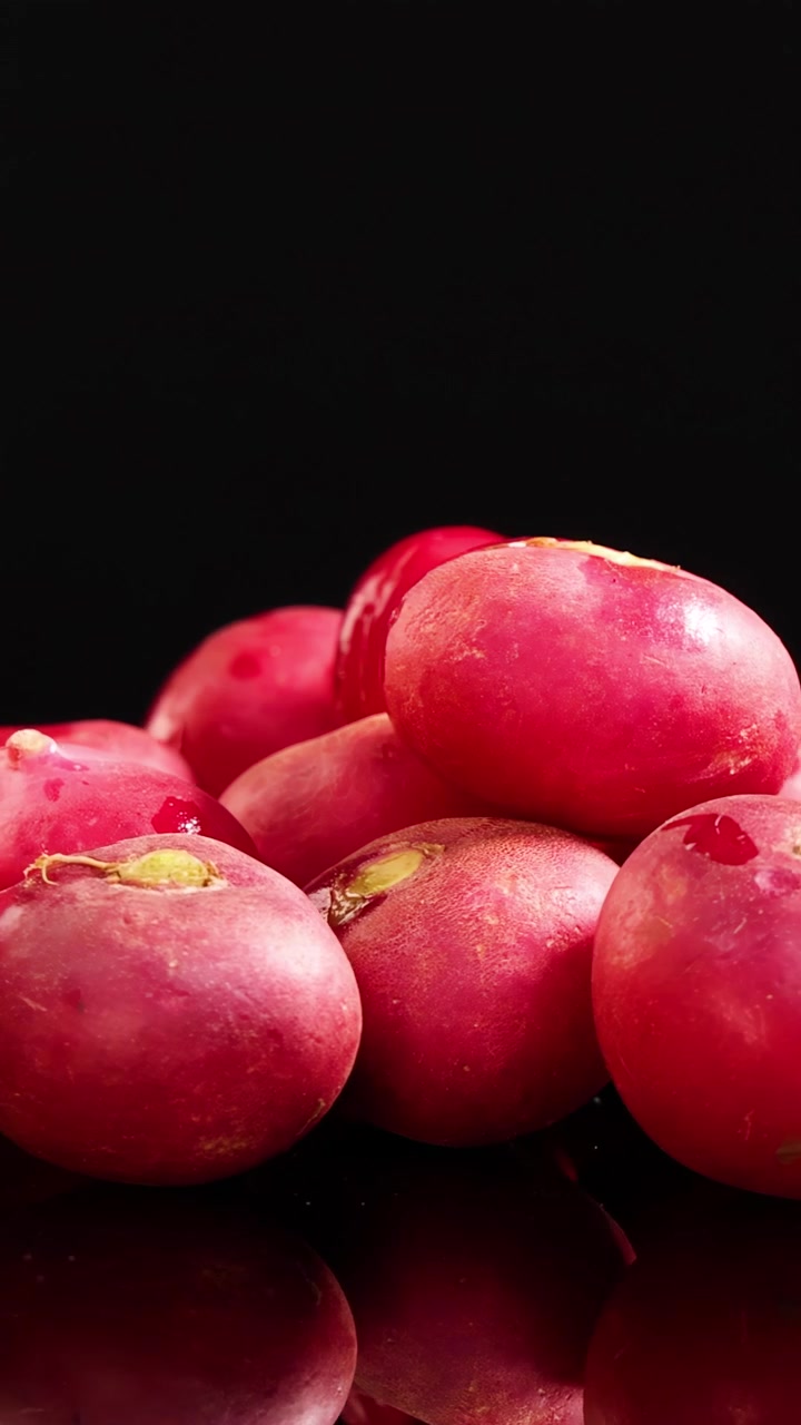 A pile of fresh red radishes rotates slowly on a glossy black surface, illuminated by bright studio lighting, highlighting texture and vibrant color