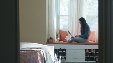 girl on bedroom window bench, working on computer