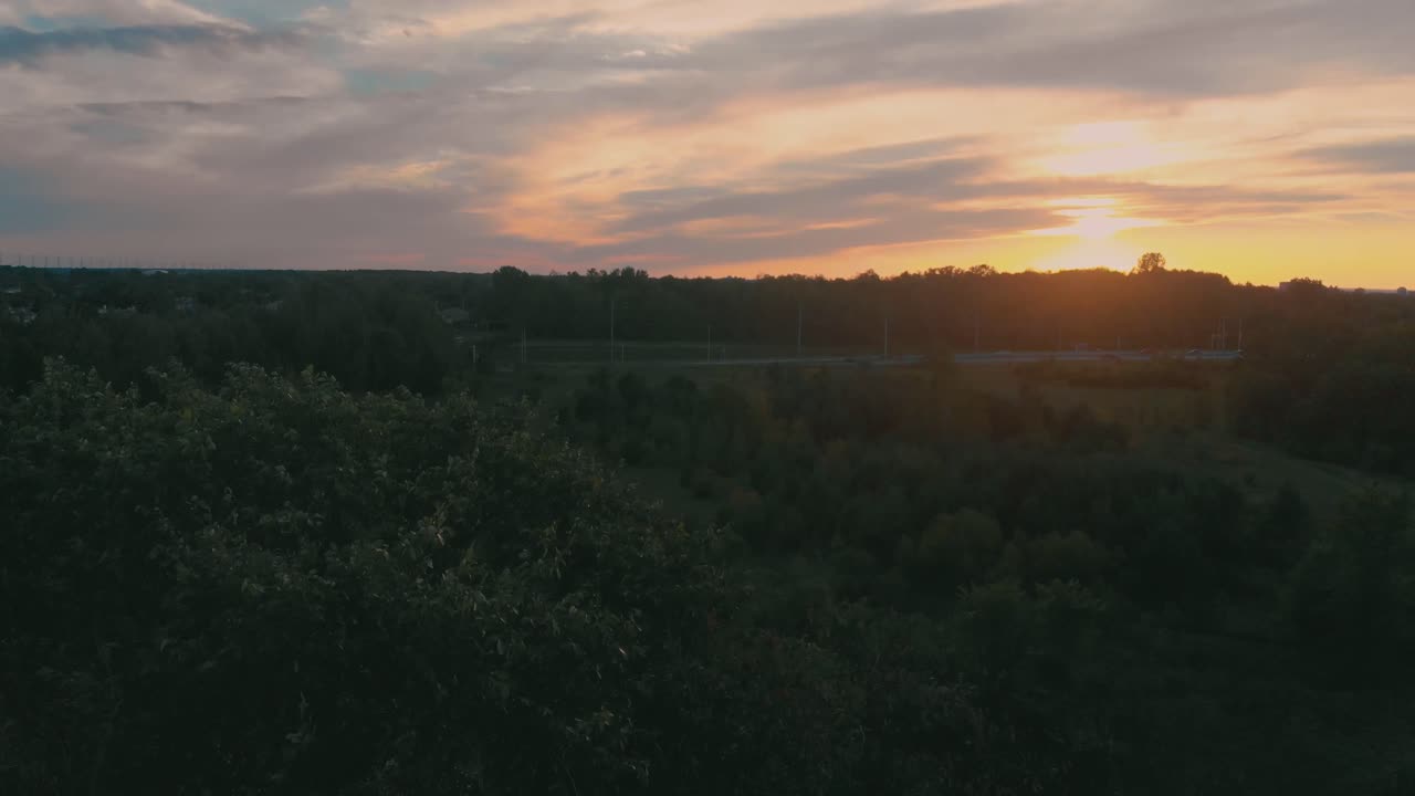 日没時にオンタリオ州ネピアン市郊外の高速道路に向かう木の上をゆっくりと空中飛行し、丘と木々の上に太陽が輝いています
