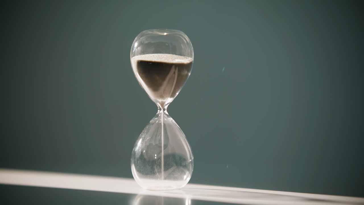 Closeup hand turning hourglass starting new countdown in sunlight. Sand flowing