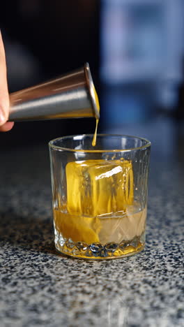 yellow thick liquid in poured into the glass with ice cube in it. preparation of alcohol beverage in the bar. close up. vertical video.