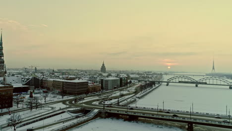 aerial drone shot of busy road and railway bridge over the frozen river and city of riga by the banks of the river in latvia 2021 on a cold wintry sunset