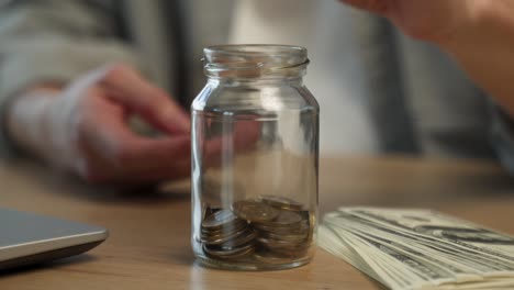 young employee throws coins in glass jar near dollar bills