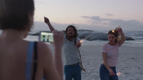 feliz grupo de amigos bailando agitando bengalas en la playa posando para video