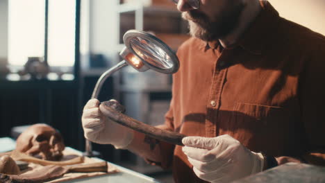 archaeologist inspecting ancient wooden artifact under magnifying lamp