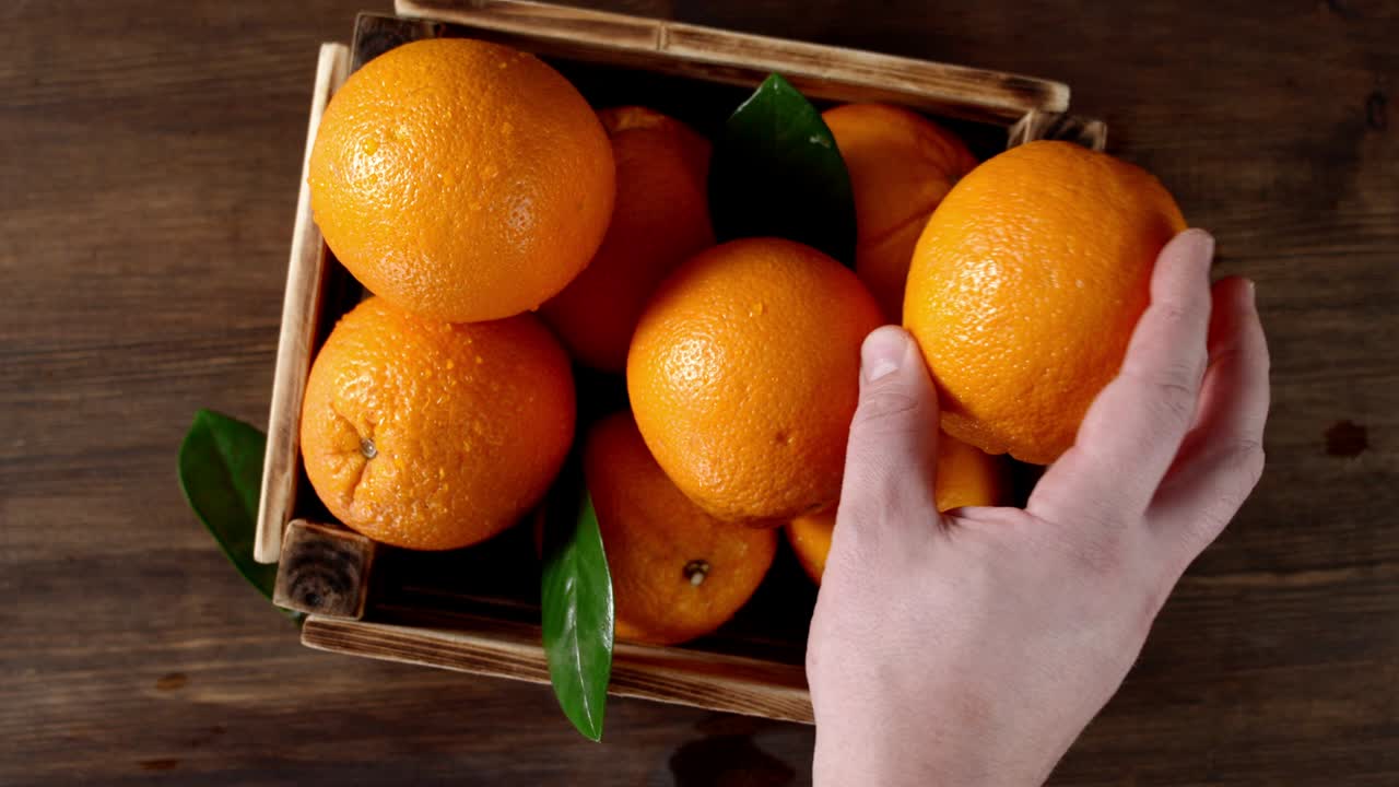 la mano masculina pone naranjas en una caja de madera.