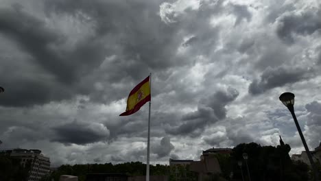 Low-angle-view-of-the-Spanish-flag-under-a-dramatic-clouded-changing-sky