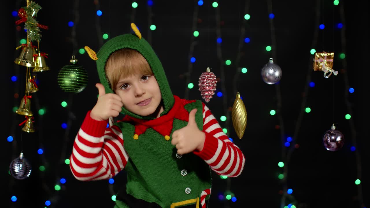Náctiletá dívka v kostýmu vánočního elfa / pomocníka Santa Clause ukazuje palec nahoru na černém pozadí