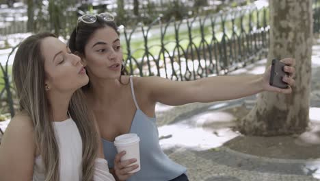 mujer muy joven sentada en un banco en el parque de la ciudad y tomando una foto selfie