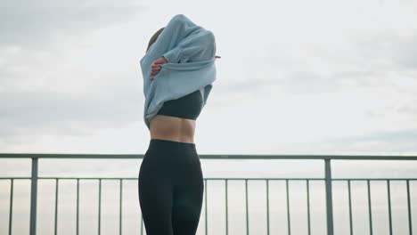 woman standing beside iron fence, removing hoodie with a smile on her face, she is in an outdoor setting with a calm expression, perfect for fitness, lifestyle, and outdoor moments