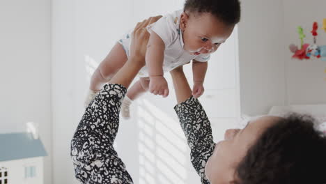 mother cuddling and playing with baby son in nursery at home lifting him in air