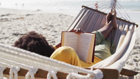 african american woman reading and lying in hammock on sunny beach