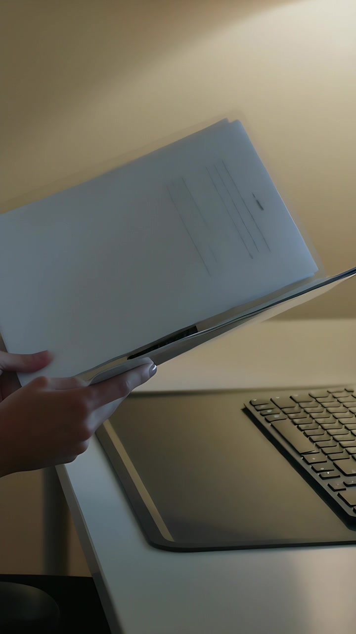 Vertical video: Rotating hands entering left holding paper stack over keyboard, organizing with pen
