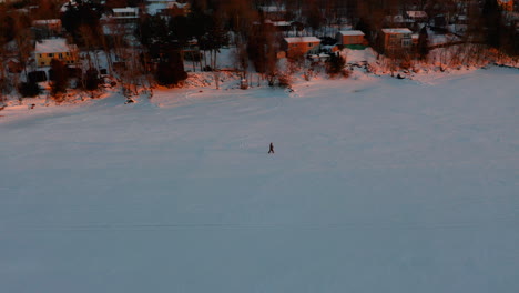 一名人在日落时沿着一条冻结的河流滑雪的空中景象