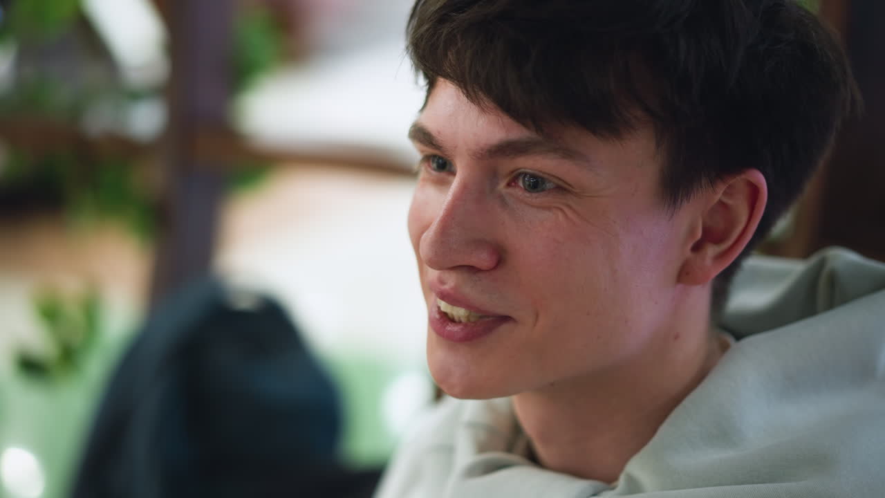 Closeup of European man smiling while talking with fellow, friendly eye contact, visible teeth, indoor setting with soft background blur, warm expression conveying camaraderie and conversation