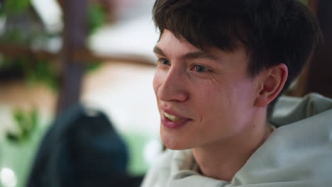 closeup of european man smiling while talking with fellow, friendly eye contact, visible teeth, indoor setting with soft background blur, warm expression conveying camaraderie and conversation
