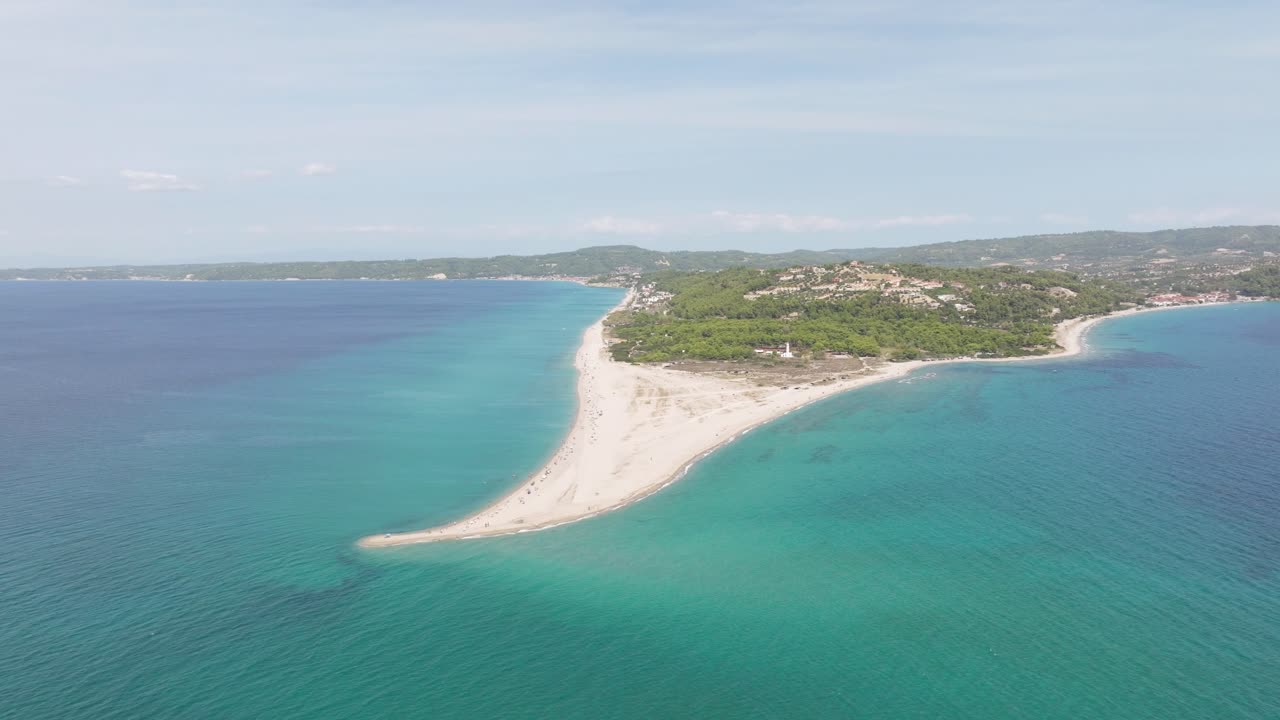 Aerial view of the narrow sandy peninsula at Possidi Cape, Greece, surrounded by turquoise waters and lush greenery under a bright, clear sky.