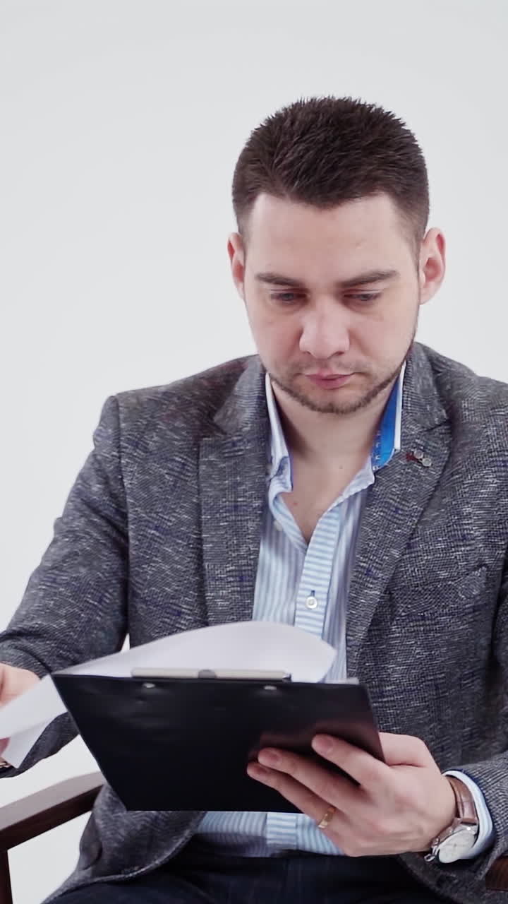 Handsome man in grey costume holding a folder. Young businessman sitting in the chair and reading documents. Slow motion. Vertical video