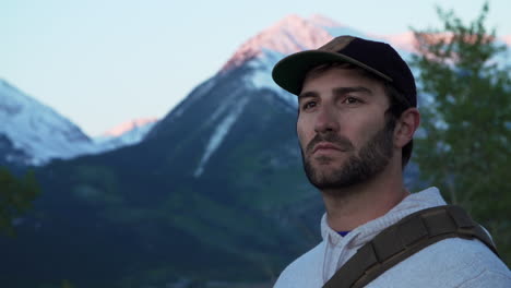 close up of an outdoorsman millennial looking on as the sun just begins to cast a pink glow on the snow-capped mountains in the background