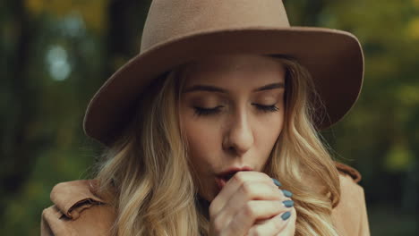 close-up view of caucasian blonde woman in a hat warming her hands in the park in autumn