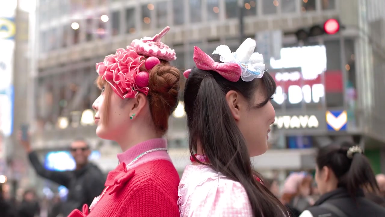Unge kvinder iført farverig pink decora-stil mode står midt i de travle menneskemængder ved Shibuya Crossing.