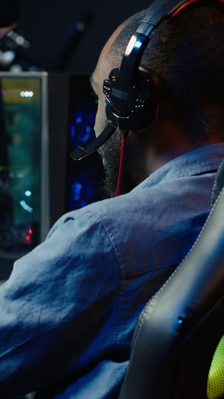 Vertical video Man playing SF shooter videogame, talking into headset with friends