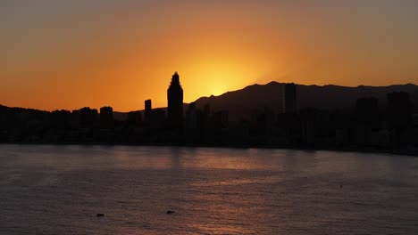 aerial view of seaside coastal city silhouette at sunset with golden orange sky, benidorm spain