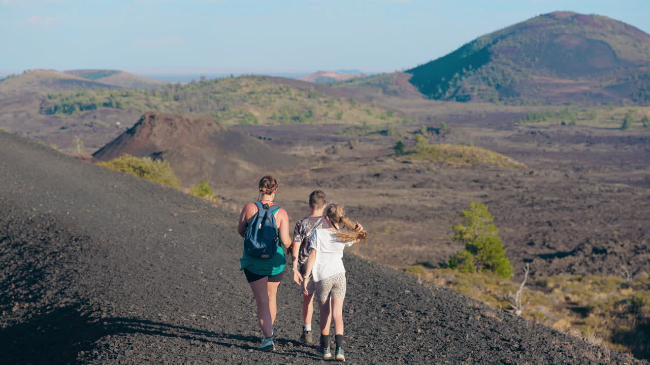 People hiking on a volcanic trail through a vast, rugged landscape