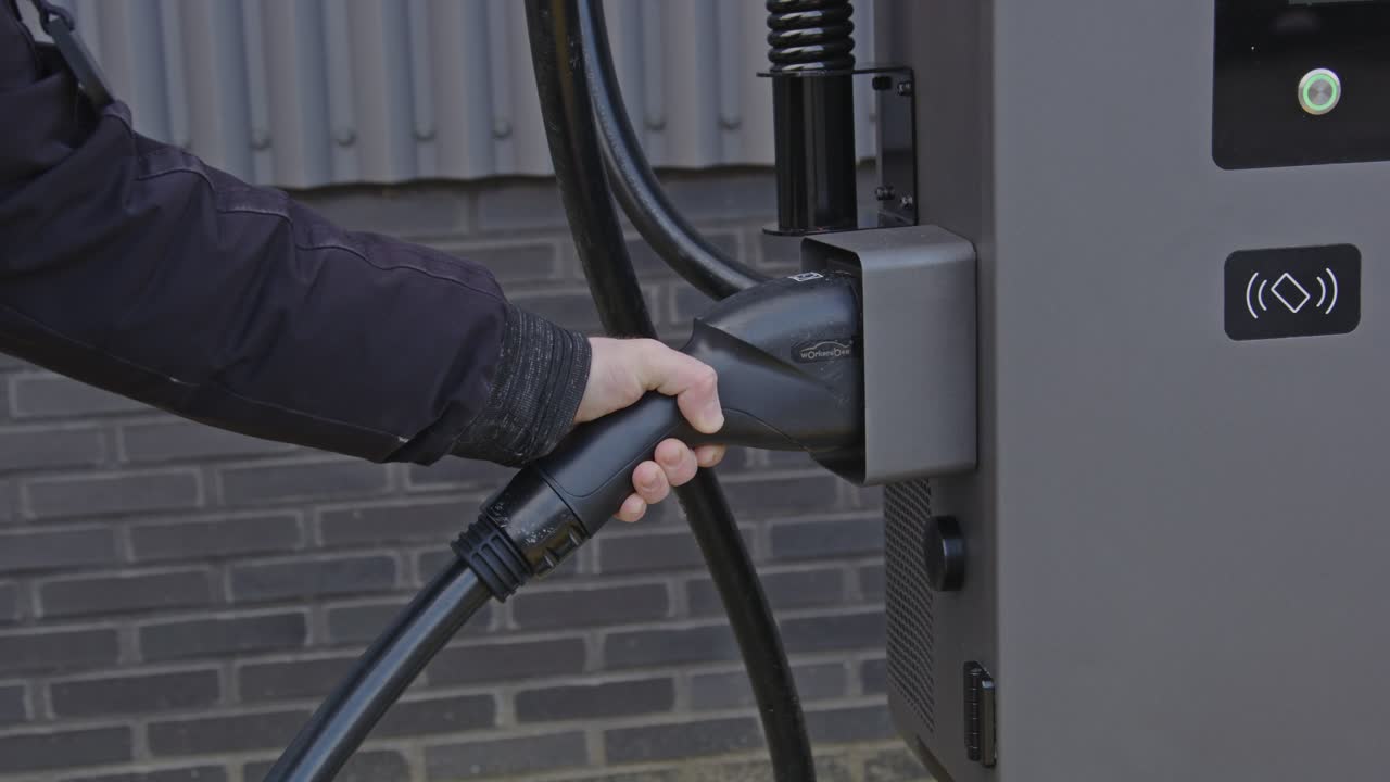 Hand returning the plug of an electric vehicle charging station back into it's dock