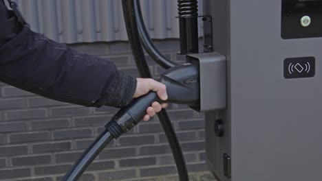 hand returning the plug of an electric vehicle charging station back into it's dock