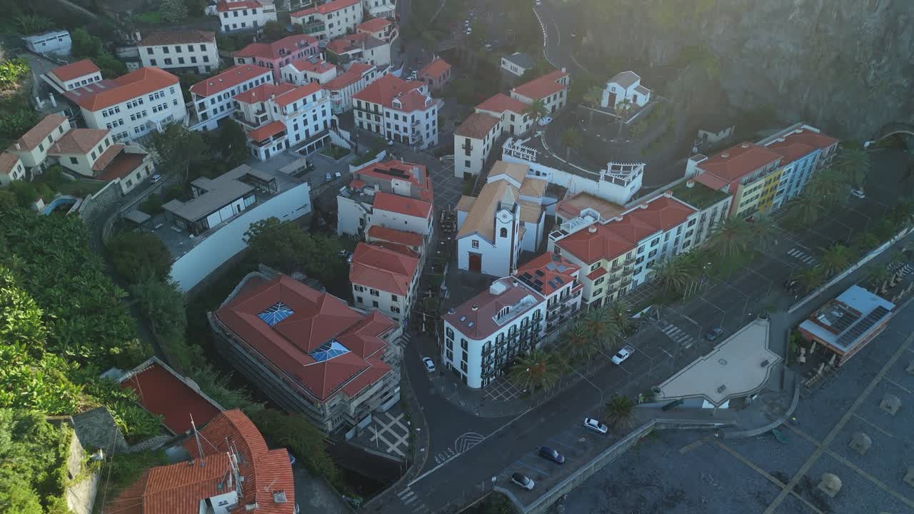 picturesque village and coastline of Ponta do Sol in Madeira, tilt up overview drone perspective, aerial shot with warm dawn colors along hazy cliffs and ocean