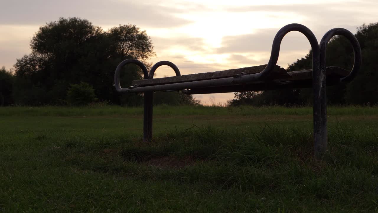 Lonley wooden park bench at sunset wide panning shot