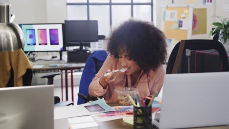 african american female designer using smartphone during lunch in casual office, slow motion