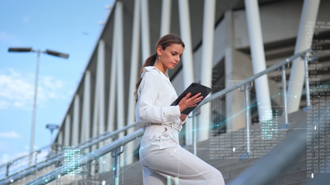 mujer de negocios en un elegante traje de oficina se encuentra afuera en las escaleras frente al edificio de oficinas y trabaja en una tableta con gráficos digitales desvanecidos como animaciones gráficas en movimiento