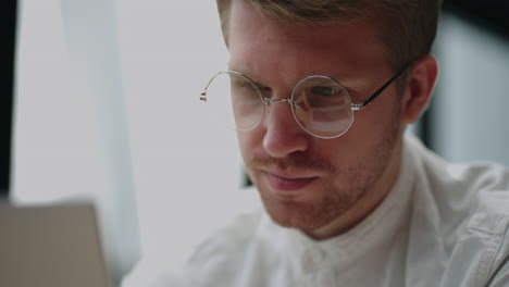 handsome man with glasses is reading news on display of laptop in office closeup view of face lawyer or businessperson