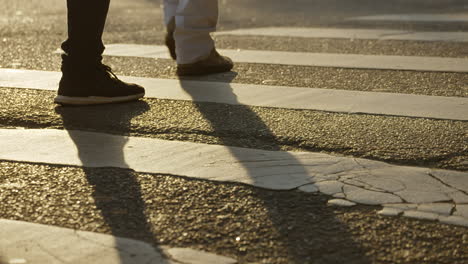 pedestrians crossing a street by the crosswalk under the sunset golden light filmed in slow motion in 4k high definition