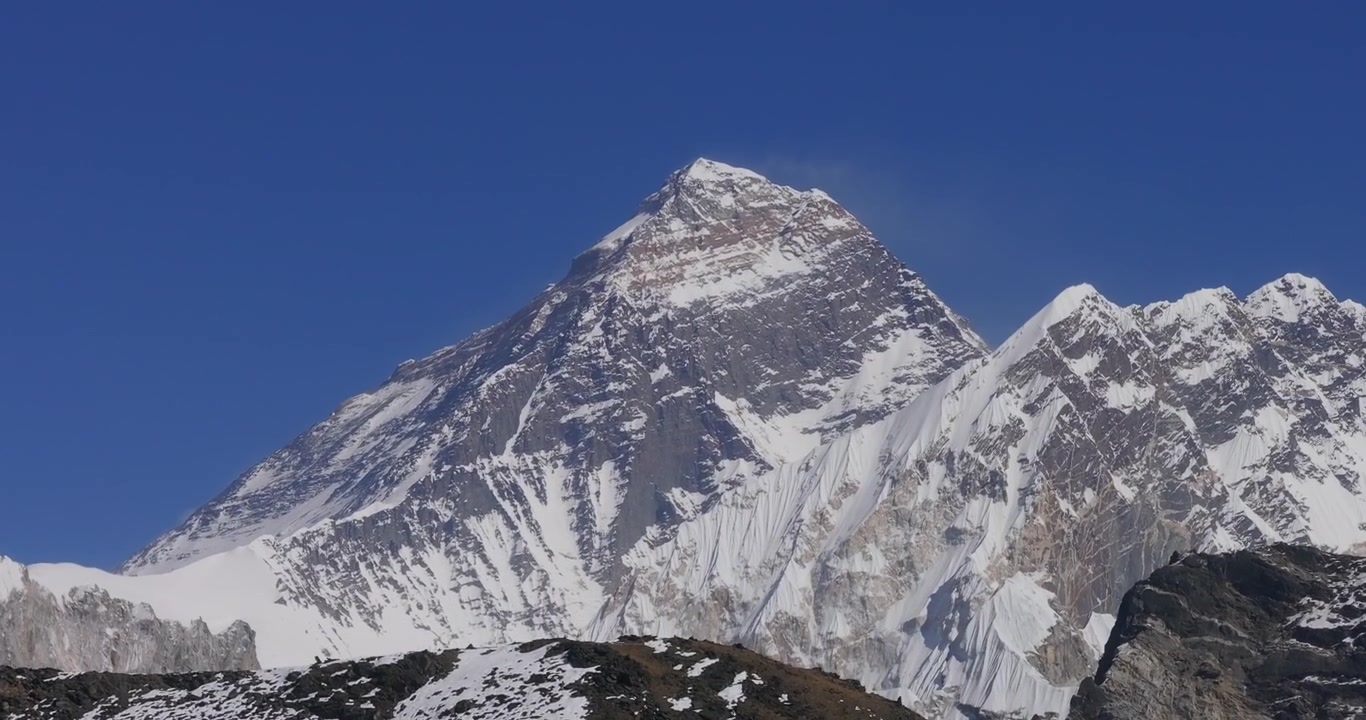 Vista aerea che rivela il Monte Everest che svetta sopra una cresta rocciosa frastagliata in Nepal, mostrando paesaggi himalayani innevati sotto un cielo azzurro limpido.